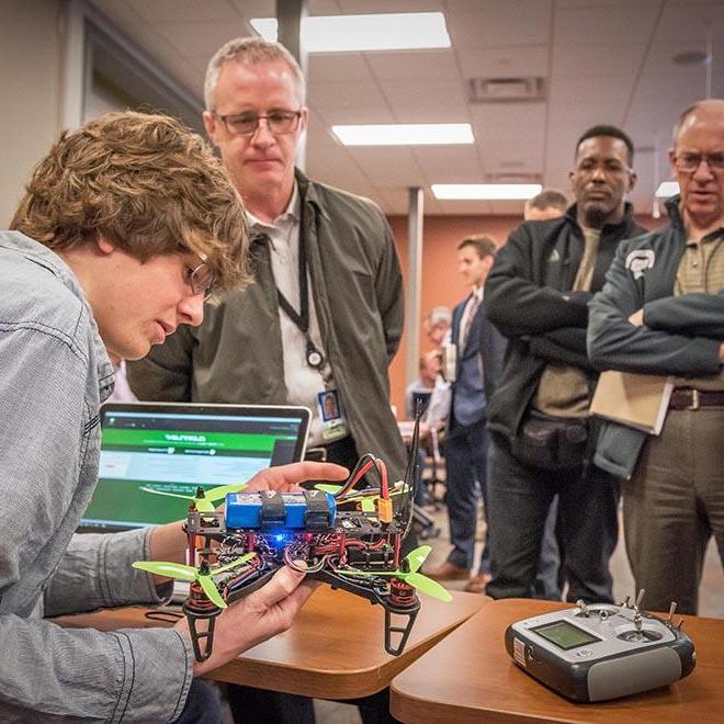 Engineering student showing his invention to three leaders.